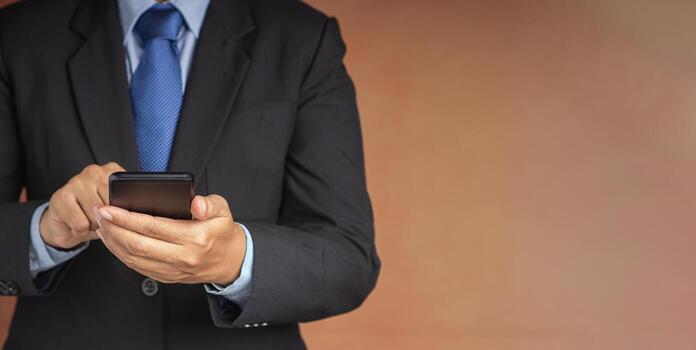 Businessman using a smartphone while standing with a brown background. Space for text. Communication and technology concept photo