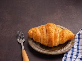 Top view of croissant milk on a plate, cutlery, and a cloth placed on the old kitchen table. Space for text. Concept of dessert and relaxation photo