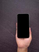 Close-up of a smartphone with blank screen on the palm hand with a gray stone background. Technology and communication concept photo
