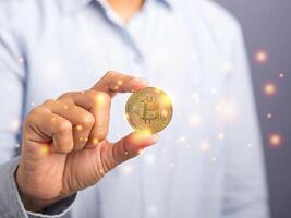 Businessman showing a bitcoin gold coin with sunlight effect while standing with a gray background. Close-up photo. Space for text. Virtual cryptocurrency and future money concept photo