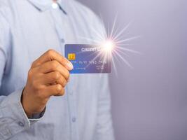 Midsection of a businessman wearing a light blue shirt holding a mockup blue credit card with star light effect while standing in a studio with copy space for text. Money and business concept photo