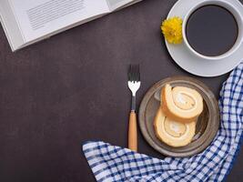 Top view of a book with roll cakes on a plate, a white coffee cup, and a cloth placed on dark gray stone background. Space for text. Concept of relaxation photo
