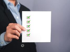 Midsection of a businessman holding a white paper with a checklist against a gray background photo
