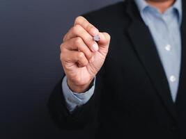 A businessman wearing a suit is holding a pen write or writing on the virtual screen or in the air against a gray background. Space for text. Close-up. Modern business background concept photo