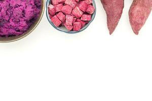Purple yams whole, sliced square in a bowl, and mashed potatoes on the dish placed on a white background. Space for text. Purple sweet potatoes. Top view. Vegan fruit and healthy fruits concept photo