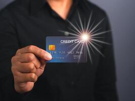 Portrait of a businessman wearing a black shirt holding a mockup blue credit card with star light effect while standing in a studio with copy space for text. Money and business concept photo