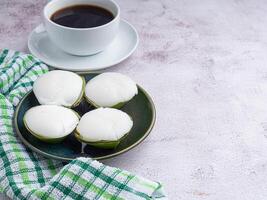 Thai pudding with coconut topping on a plate with a white coffee cup, and a cloth placed on a gray stone background. Space for text. Top view. Beverage, dessert, and relaxation concept photo