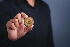 Investor guy showing a bitcoin golden coin with a dark gray background. Close-up photo. Space for text. Virtual cryptocurrency and future money concept photo