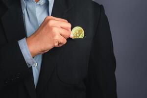 An investor guy holding a bitcoin golden coin put to suit pocket with a gray background. Close-up photo. Space for text. Virtual cryptocurrency and future money concept photo