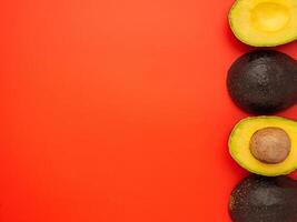 Top view of the fresh avocado whole and half placed on a red background. Organic fruit. Space for text. Concept of healthy fruits and healthcare photo
