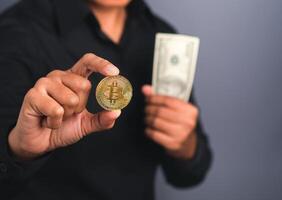 Portrait of an investor guy showing a bitcoin golden coin and US banknote with a gray background while standing in the studio. Space for text. Virtual cryptocurrency and future money concept photo