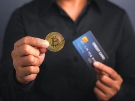 Investor guy showing a bitcoin golden coin and blue card while standing in the studio. Close-up photo. Space for text. Virtual cryptocurrency and future money concept photo