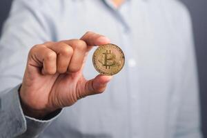 Investor guy showing a bitcoin golden coin with a gray background. Close-up photo. Space for text. Virtual cryptocurrency and future money concept photo