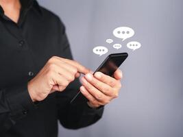 Businessman using a smartphone with an conversation icon while standing with a gray background. Space for text. Communication and technology concept photo