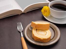 Top view of a book with roll cakes on a plate, a white coffee cup, and a cloth placed on a dark brown background. Space for text. Concept of reading and relaxation photo