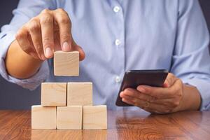 Hand holding a smartphone and blank wooden blocks while sitting on a chair. Close-up photo. Space for text photo