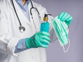 Close-up of hands doctor's wearing gloves and holding a face mask while standing on a gray background. Space for text. Concept of healthcare photo