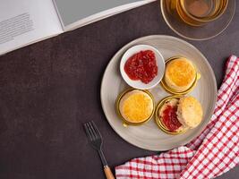 English style scones delicious freshly baked homemade with strawberry jam on a plate and cutlery with a cloth placed on the old kitchen table. Top view with copy space for text. Flat lay photo