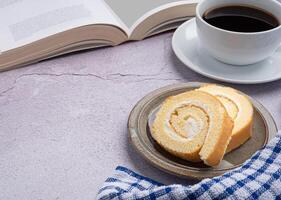 Top view of a book with roll cakes on a plate, a white coffee cup, and a cloth placed on a gray stone background. Space for text. Concept of relaxation photo