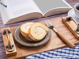 Top view of roll cake on a plate on a wooden tray with a cloth and a white coffee cup placed on a wooden table. Space for text. Concept of relaxation photo