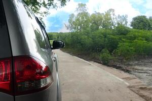 Rear side of grey car stop on the road. Car driving on concrete road in the contryside. Beside with nature of green trees. with the bright sunshine time. photo