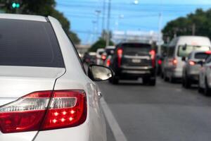 Luxury of white car stop on the asphalt road. Traveling in the provinces during the bright period. Open light brake. Many cars rushed forward in a long queue. photo