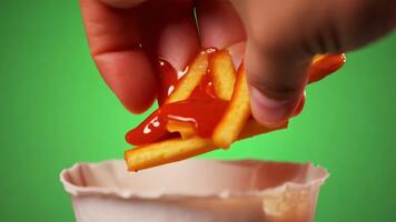 A hand dipping a crispy French fry into a ketchup cup. Green screen backdrop. Soft, ambient lighting to create a fast-food feel. video