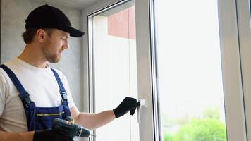 Worker in overalls installing a window lock for home safety. The concept of protecting a child from falling out of windows. Handle with a lock on the window video