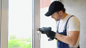 Worker in overalls installing a window lock for home safety. The concept of protecting a child from falling out of windows. Handle with a lock on the window video