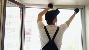 Service man in uniform installing pvc window with measure tape in house video