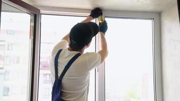 Service man in uniform installing pvc window with measure tape in house video
