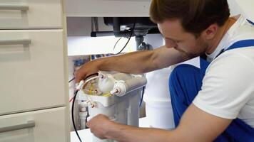 Repairman installing water filter cartridges in a kitchen. Installation of reverse osmosis water purification system video