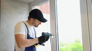 Worker in overalls installing a window lock for hotel room safety. The concept of protecting a child from falling out of windows. Handle with a lock on the window video