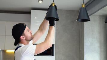Electrician in uniform installs lamp lighting and spot loft style on ceiling video