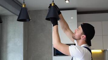 Electrician in uniform installs lamp lighting and spot loft style on ceiling video