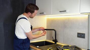 Repair of the faucet in the kitchen near the sink. A plumber in the kitchen installs a new water tap video