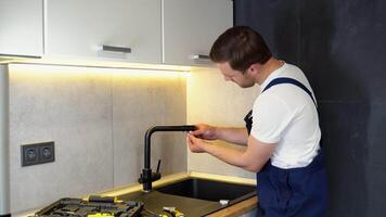 Repair of the faucet in the kitchen near the sink. A plumber in the kitchen installs a new water tap video