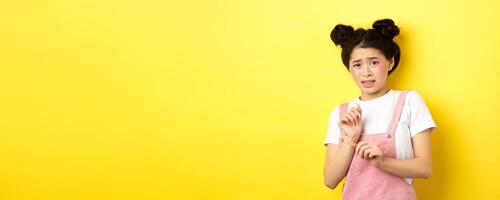 Stay away. Reluctant timid asian girl step back, raising hands to block something disgusting, grimacing displeased, say no, rejecting with aversion, yellow background photo