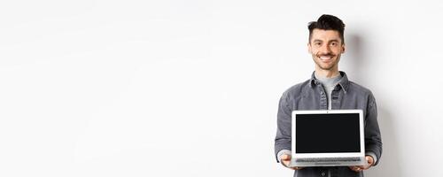 Smiling young man showing empty laptop screen, showing online deal, standing on white background photo