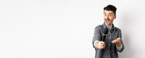 Handsome smiling man stretch out hand with microphone, giving you mic, standing on white background photo