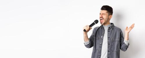 Handsome guy singing in mic with passion, perform for audience, holding microphone and gesturing, standing on white background photo