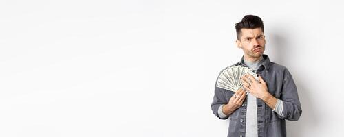 Greedy guy frowning and hugging dollar bills, unwilling to share money, standing on white background photo