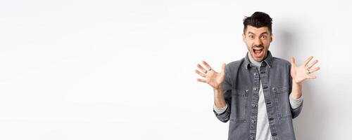 Angry man scream and look scary at camera, shouting with furious and hateful expression, standing on white background photo