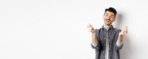 Handsome smiling man showing hand hearts and looking with love at camera, standing on white background photo