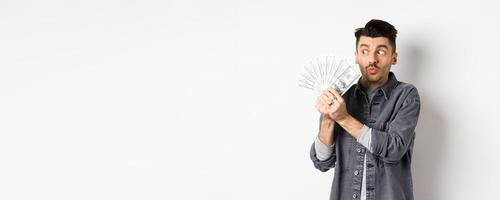 Excited man hugging and kissing dollar bills, holding money and rejoicing, standing on white background photo