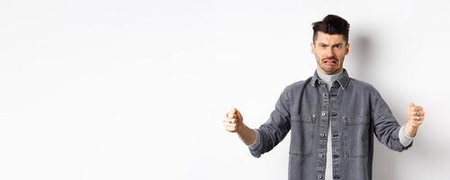 Disgusted guy showing big size object and grimacing from dislike and aversion, talking about disgusting large thing, standing on white background photo