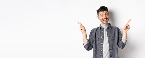 Cheerful smiling man pointing fingers sideways, showing left and right ways, looking happy at camera, standing on white background photo