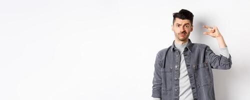 Disappointed guy showing small size and grimacing upset, frowning displeased with little thing, standing on white background photo