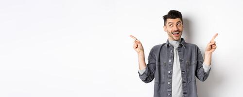 Happy stylish guy laughing and pointing sideways, showing two choices, demonstrate promo offers and smiling, standing against white background photo