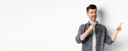 Handsome smiling guy making announcement, winking and pointing at upper right corner, showing logo, inviting to check out advertisement, standing on white background photo